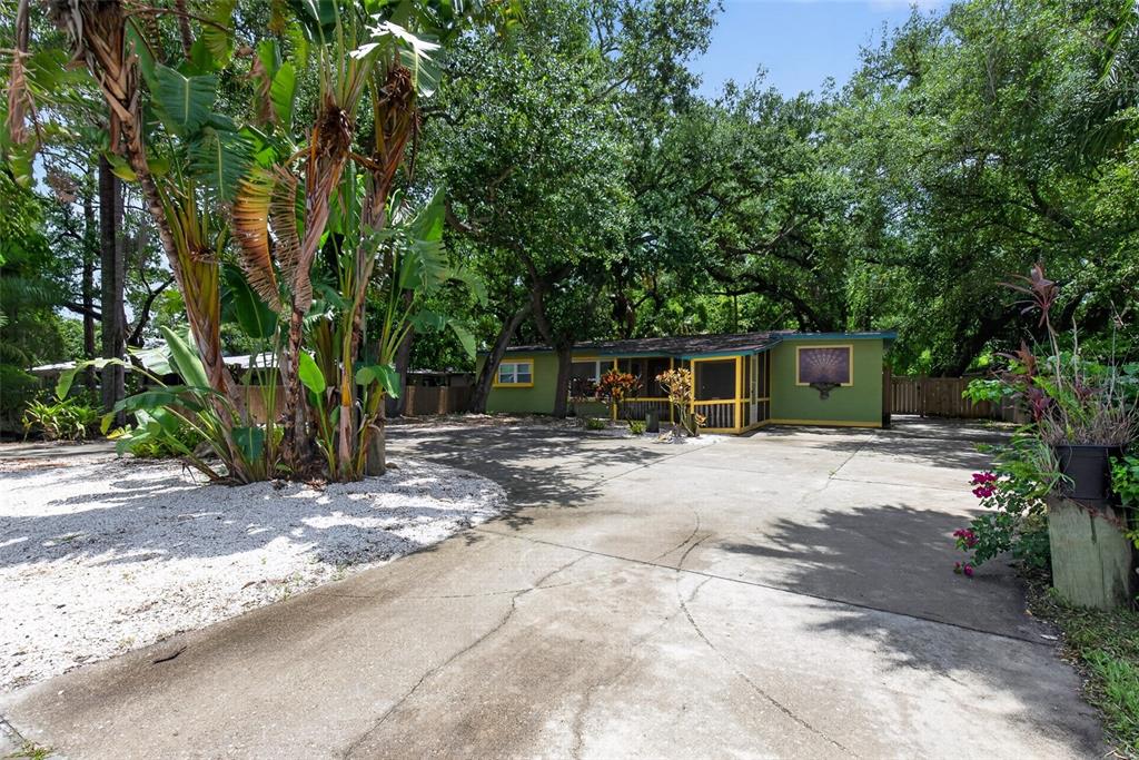 A green one-story house with a screened porch sits behind a large concrete driveway — 6270 62ND AVENUE N, PINELLAS PARK, FL