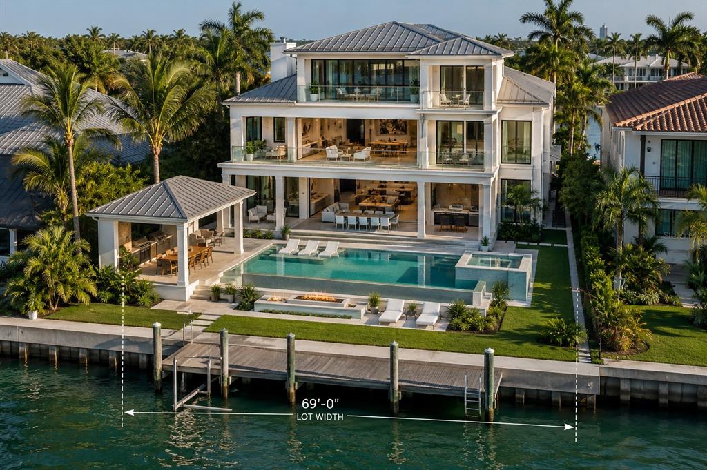 An aerial view of a three-story waterfront home with a pool, dock, and patio — 11245 9TH STREET E, TREASURE ISLAND, FL