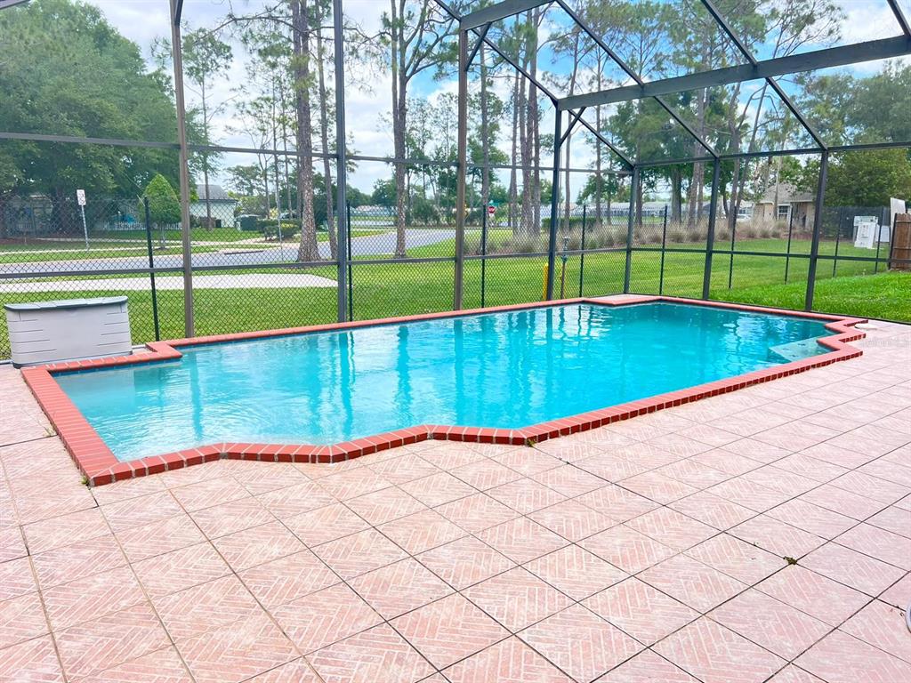 A rectangular swimming pool with red brick coping sits on a tiled patio inside a screen — 4627 EAGLET LANE, KISSIMMEE, FL