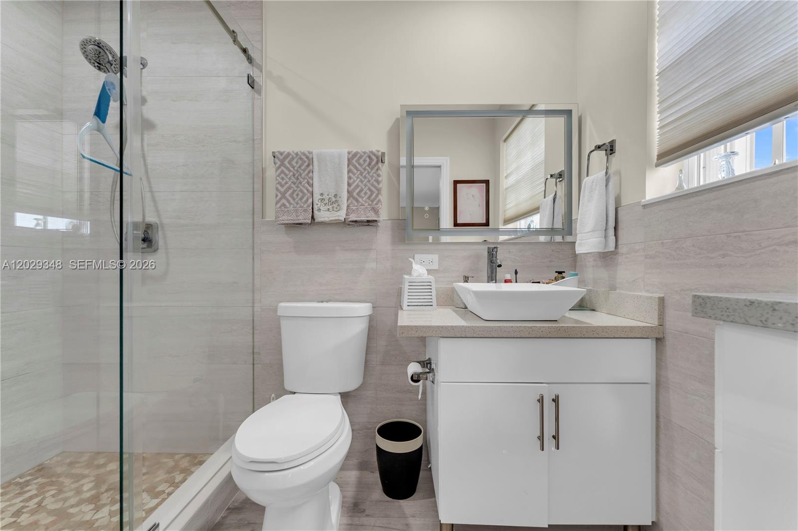 A modern bathroom features a glass-enclosed shower, a white vessel sink, and light-colored tile — 884 W 72nd Pl, Hialeah FL 33014, HIALEAH, FL