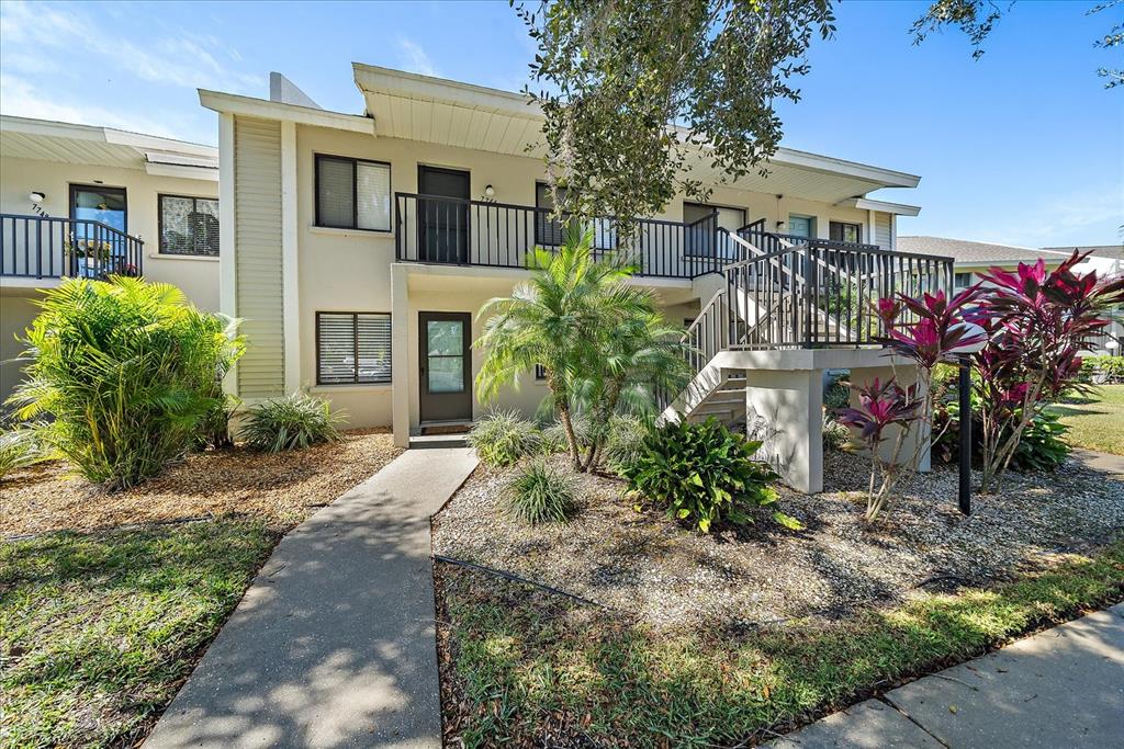 A two-story apartment building exterior with a concrete walkway, stairs, and tropical landscaping — 7742 EAGLE CREEK DRIVE UNIT 7524, SARASOTA, FL
