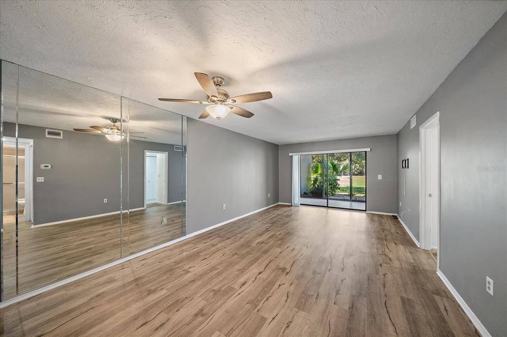 An empty living room features gray walls, wood-look flooring, a ceiling fan, and mirrored walls — 7742 EAGLE CREEK DRIVE UNIT 7524, SARASOTA, FL