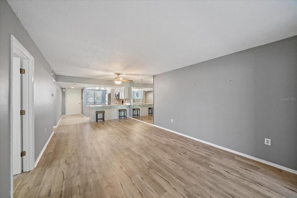 A living room with gray walls, light wood-look flooring, and a mirrored wall section — 7742 EAGLE CREEK DRIVE UNIT 7524, SARASOTA, FL