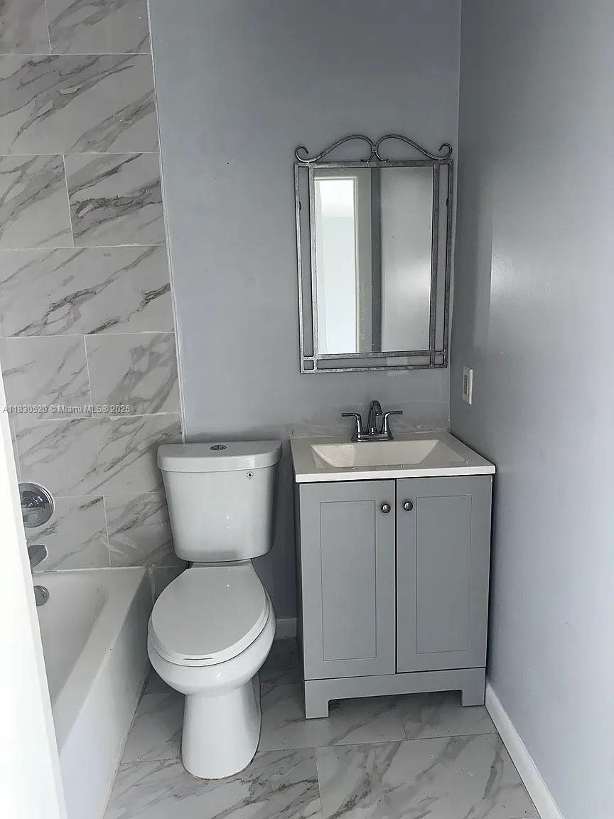 A bathroom features a gray vanity, a white toilet, and a marble-tiled bathtub surround — 4410 26th Ave # 2, Vero Beach FL 32967, VERO BEACH, FL