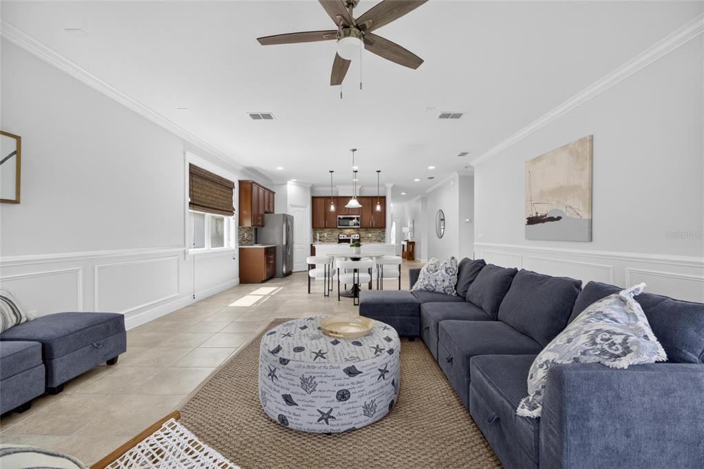 An open-concept living room and kitchen featuring a blue sectional sofa, tile floors, and cabinetry — 7328 MILESTONE DRIVE, APOLLO BEACH, FL