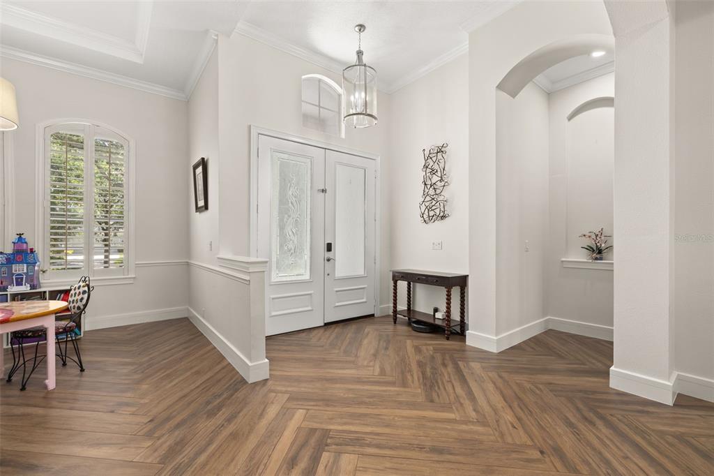 An entryway with white double doors, a chandelier, and wood-look flooring in a herringbone pattern — 8351 BOWDEN WAY, WINDERMERE, FL