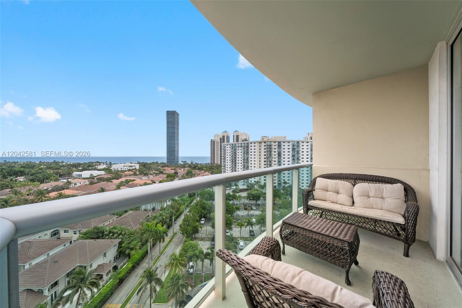 A balcony with wicker furniture overlooks a residential area and distant high-rise buildings — 19380 Collins Ave # 1224, Sunny Isles Beach FL 33160, SUNNY ISLES BEACH, FL