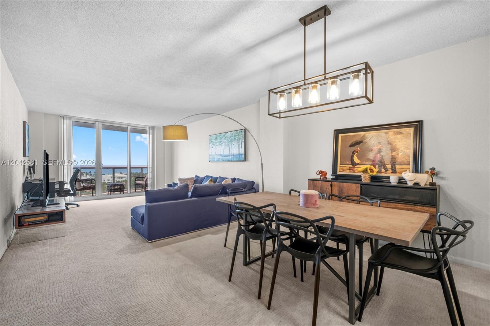 This open-concept living and dining area features a blue sofa, wooden table, and balcony view — 19380 Collins Ave # 1224, Sunny Isles Beach FL 33160, SUNNY ISLES BEACH, FL