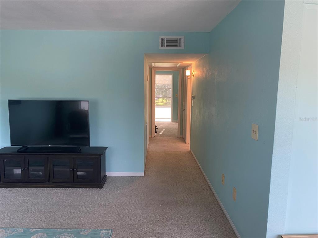 A living room with light blue walls, carpeted flooring, and a hallway leading to a doorway — 11224 82ND AVENUE UNIT 210, SEMINOLE, FL