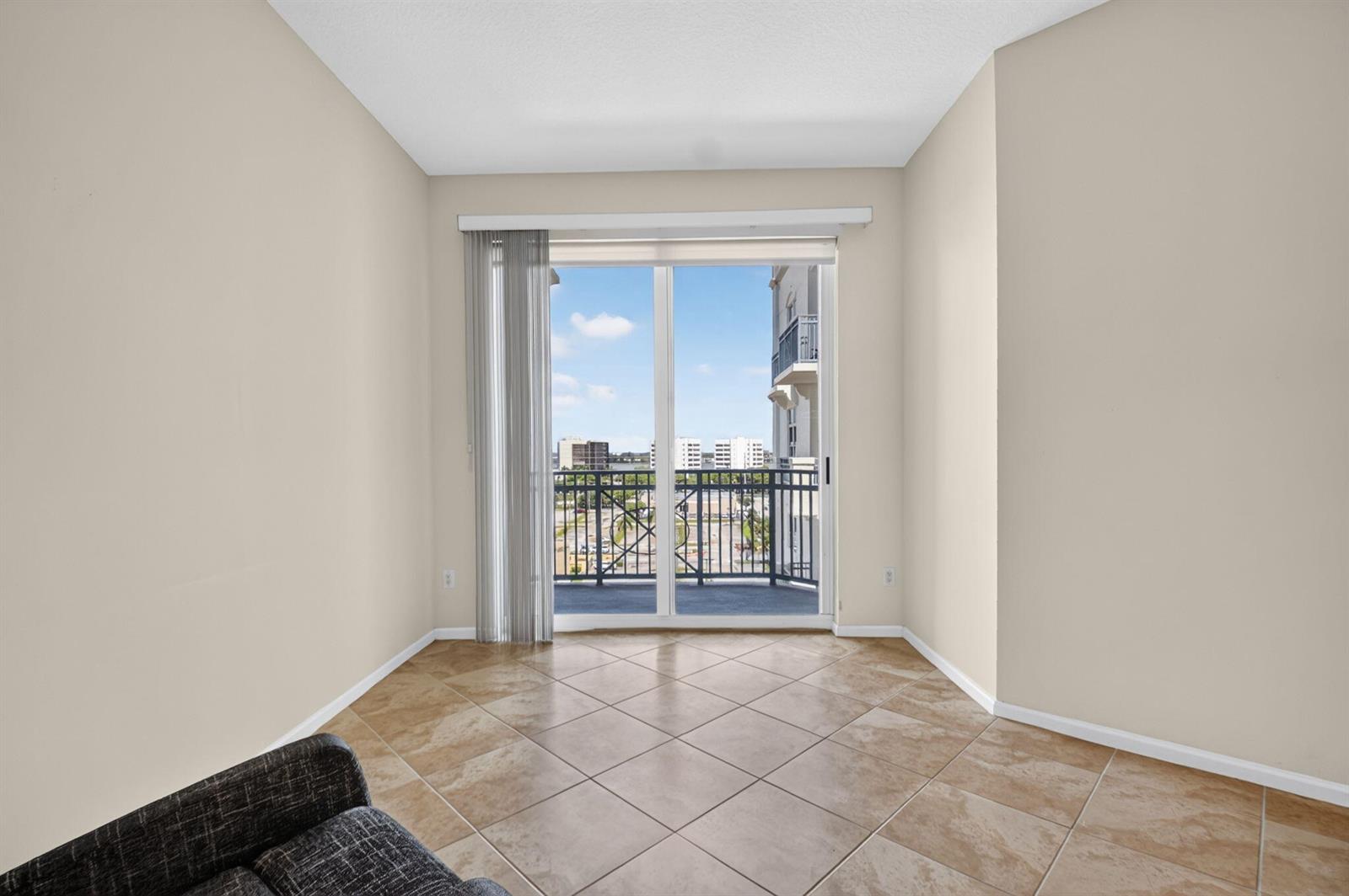 An empty room with beige walls, tile flooring, and a sliding glass door to a balcony — 403 S Sapodilla Avenue # 706, West Palm Beach FL 33401, WEST PALM BEACH, FL