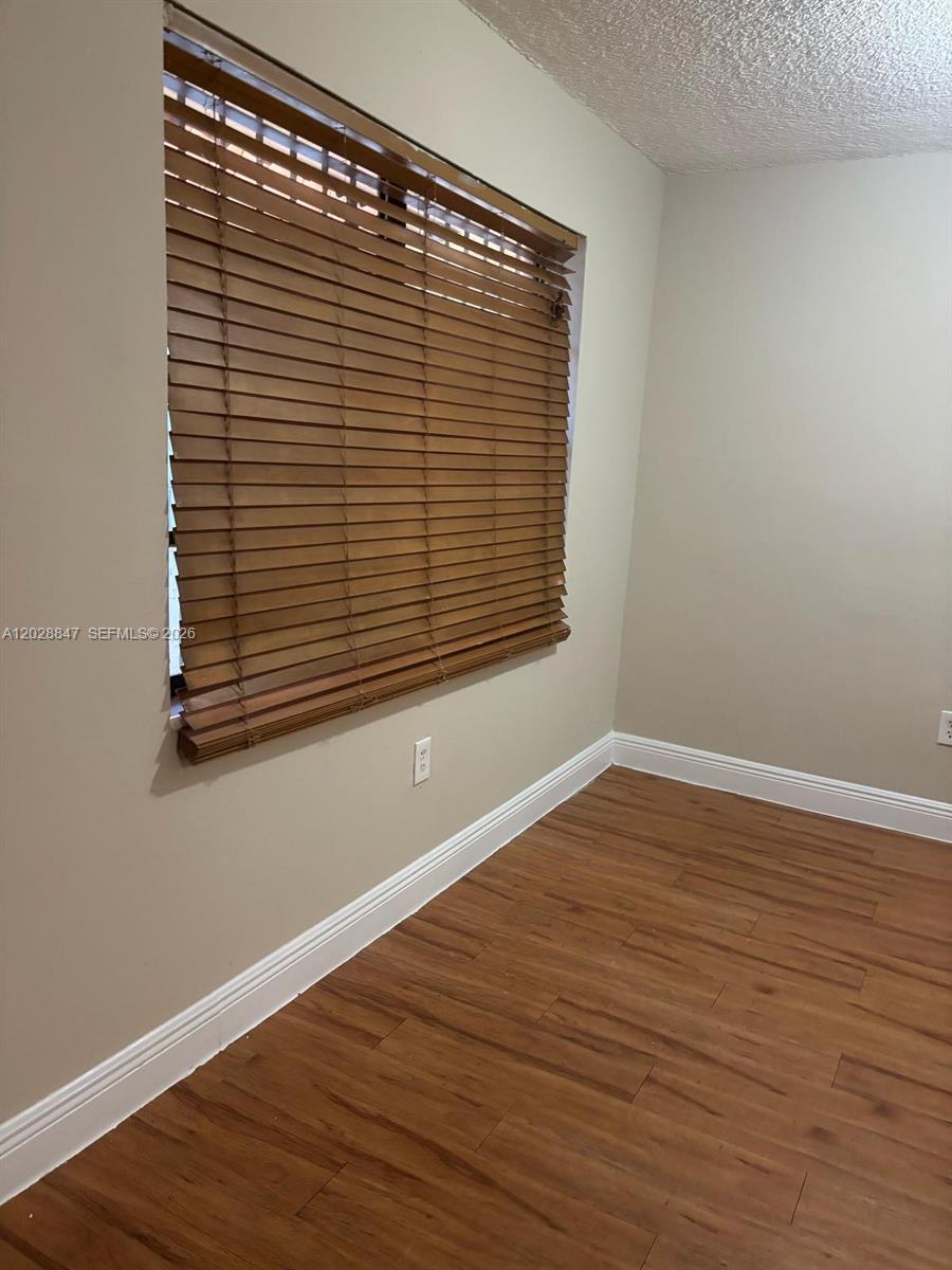 A room with wood-look flooring, beige walls, white baseboards, and wood window blinds — 6675 W 4th Ave # 408, Hialeah FL 33012, HIALEAH, FL