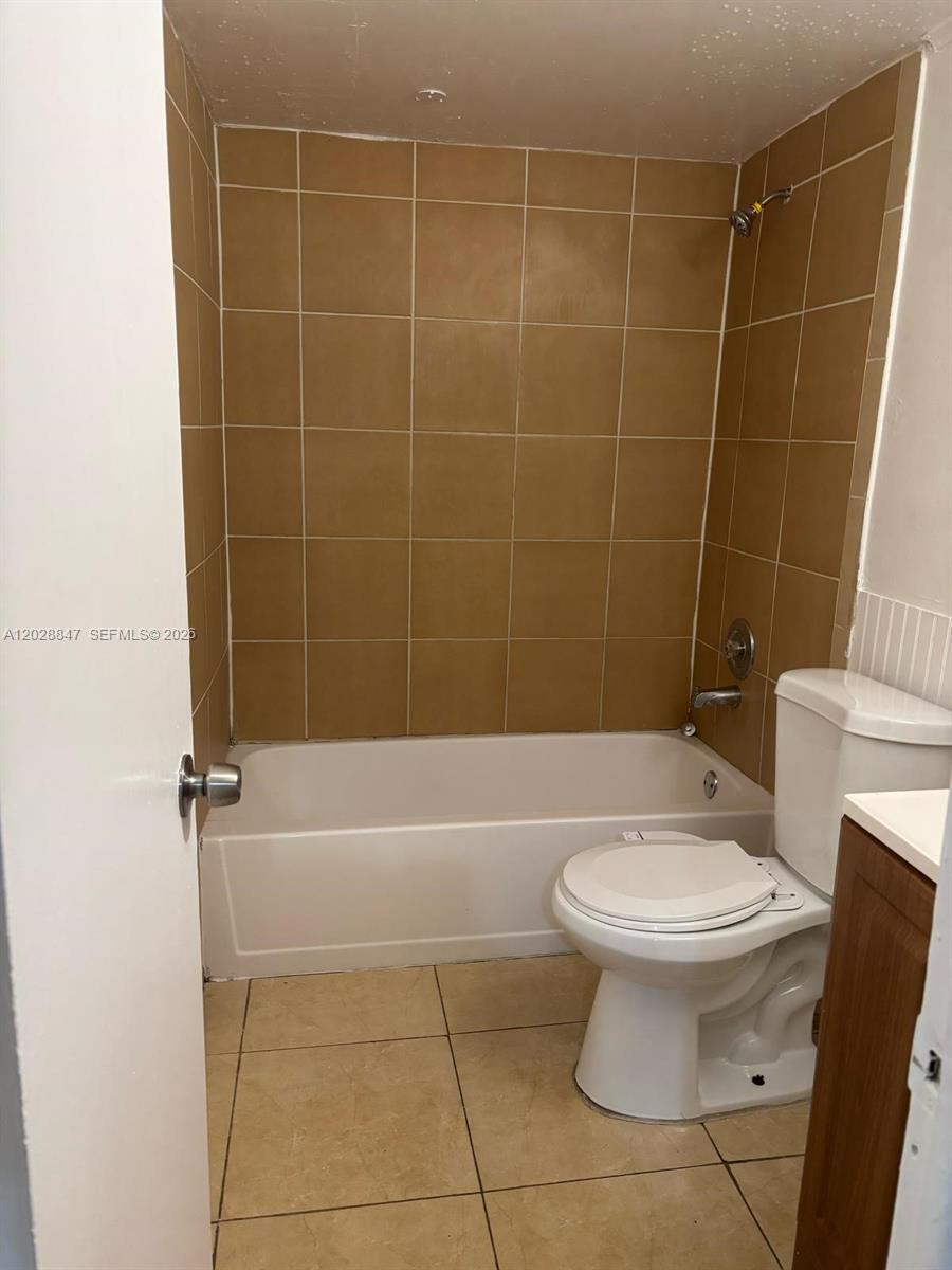 A bathroom features a white bathtub, a white toilet, and tan wall and floor tiles — 6675 W 4th Ave # 408, Hialeah FL 33012, HIALEAH, FL