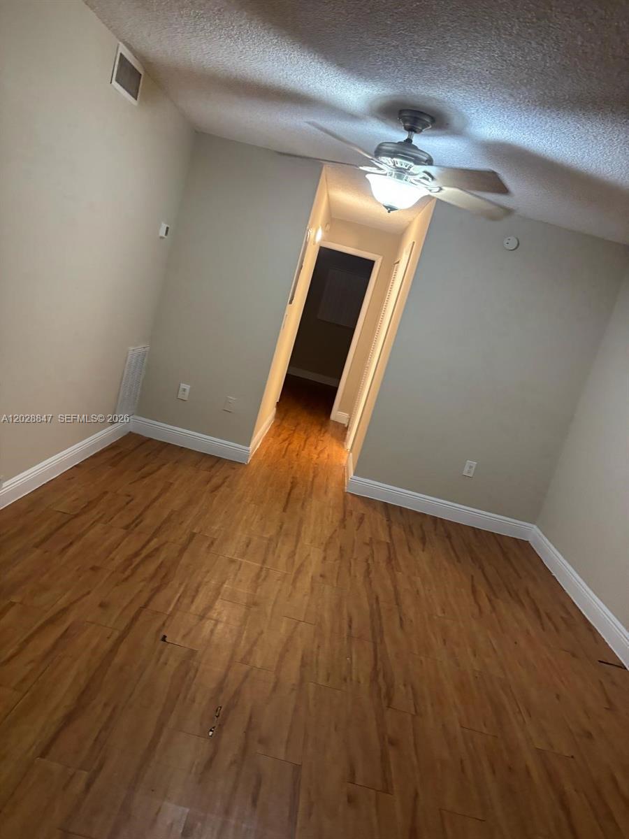 An empty room features wood-look flooring, a ceiling fan, and a doorway leading to a hallway — 6675 W 4th Ave # 408, Hialeah FL 33012, HIALEAH, FL