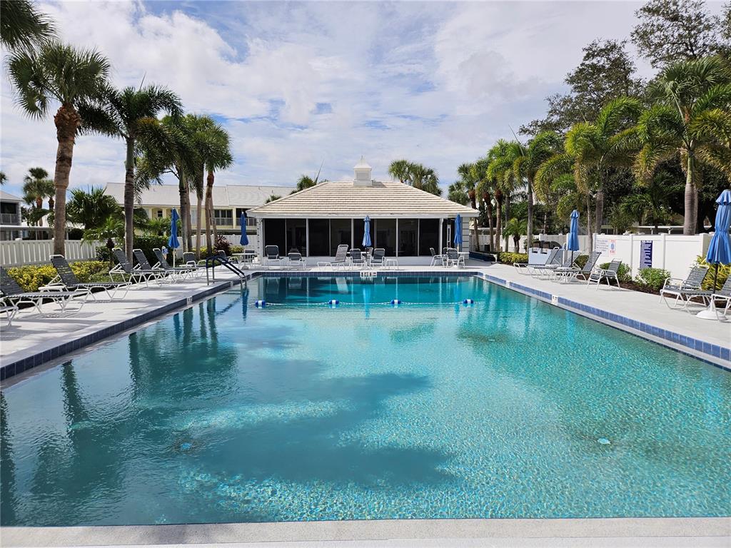 A rectangular swimming pool is surrounded by lounge chairs, palm trees, and a clubhouse building — 435 CERROMAR LANE UNIT 329, VENICE, FL