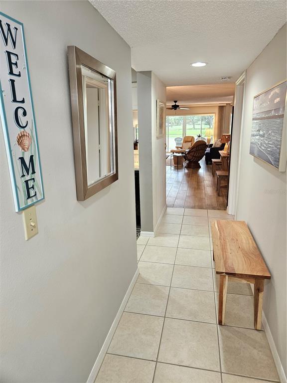 A hallway with light tile flooring leads to a living area with wood-look floors — 435 CERROMAR LANE UNIT 329, VENICE, FL