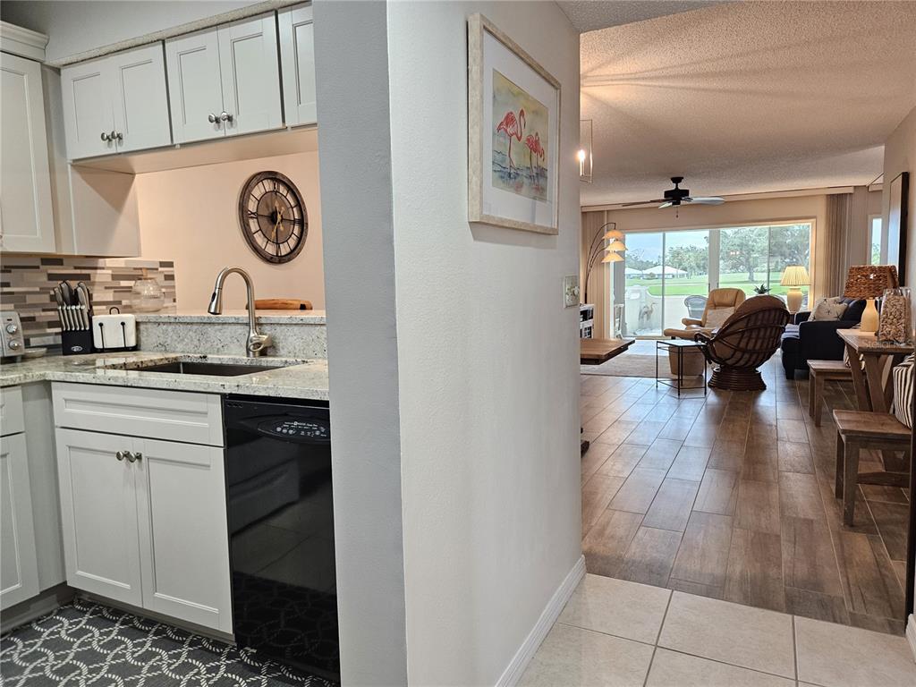 A kitchen with white cabinets and a dishwasher opens into a living area with tile floors — 435 CERROMAR LANE UNIT 329, VENICE, FL