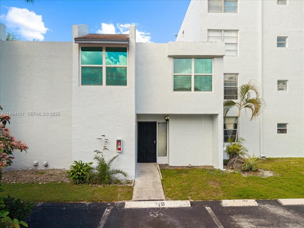 The exterior of a two-story white stucco townhouse features a black front door and parking — 9450 Live Oak Pl # 109, Davie FL 33324, DAVIE, FL