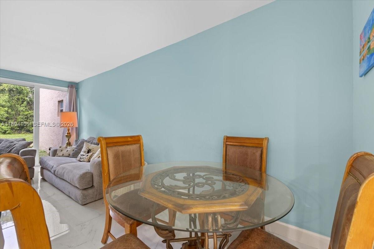 A dining area with a glass-topped table and chairs sits before a light blue wall — 9450 Live Oak Pl # 109, Davie FL 33324, DAVIE, FL