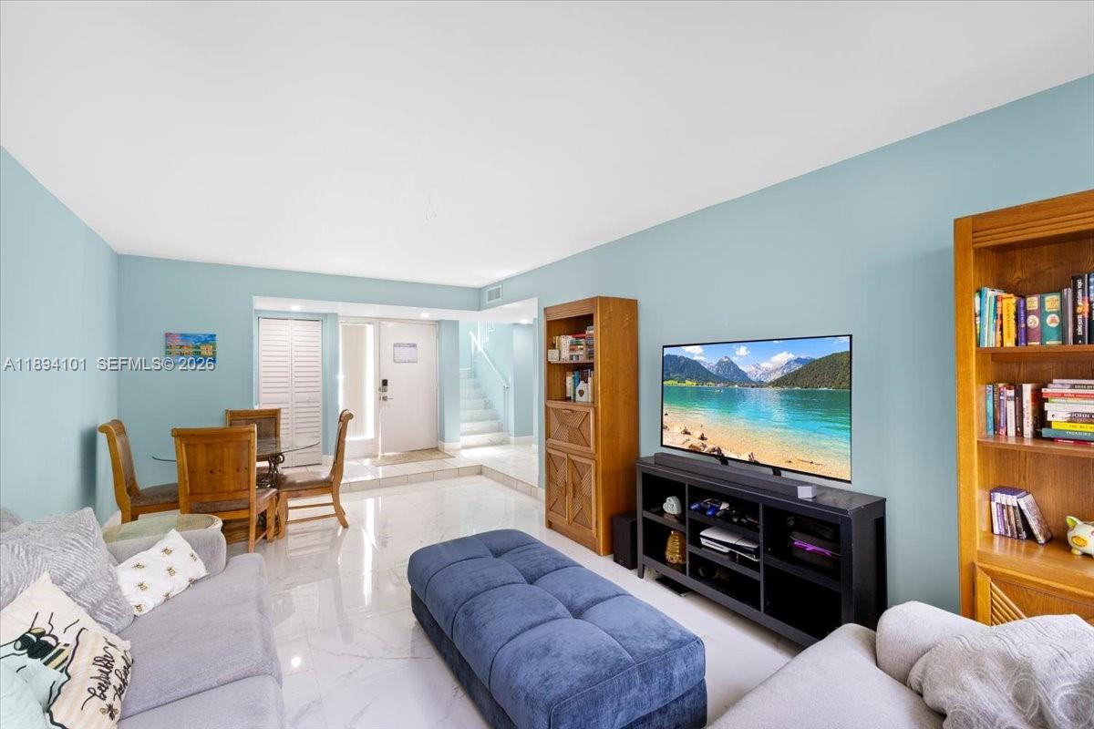 A living room features light blue walls, white tile flooring, a blue ottoman, and bookshelves — 9450 Live Oak Pl # 109, Davie FL 33324, DAVIE, FL