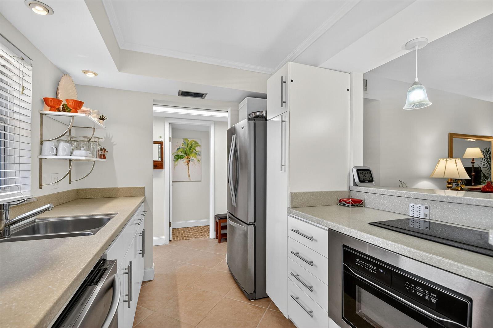 A modern kitchen features stainless steel appliances, white cabinetry, and light-colored countertops — 7 Golfs Edge # D, West Palm Beach FL 33417, WEST PALM BEACH, FL