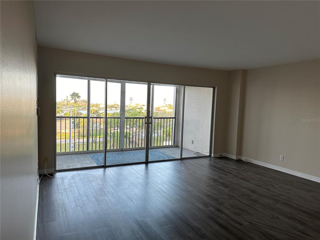 An empty room with dark wood-look flooring and a large sliding glass door to a balcony — 10355 PARADISE BOULEVARD UNIT 414, TREASURE ISLAND, FL