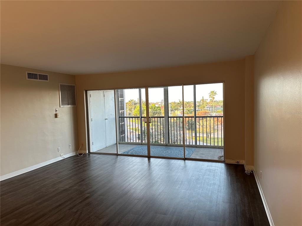 An empty room with dark wood-look flooring and a large sliding glass door to a balcony — 10355 PARADISE BOULEVARD UNIT 414, TREASURE ISLAND, FL