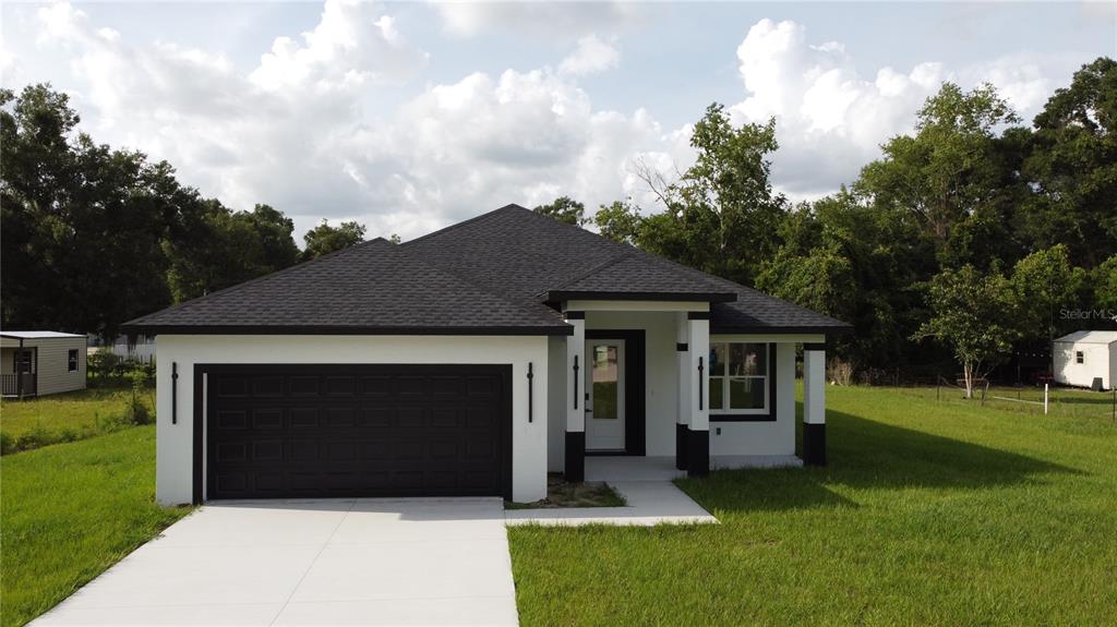 A modern, single-story house with a black roof, white stucco walls, and a two-car garage — 3649 SE 142ND STREET, SUMMERFIELD, FL