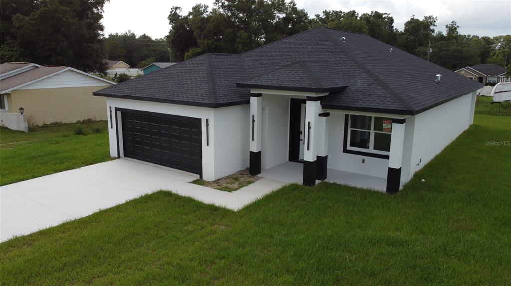 A modern single-story house with white stucco walls, a black roof, and a two-car garage — 3649 SE 142ND STREET, SUMMERFIELD, FL