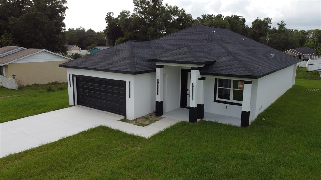 A white single-story house with a black roof and garage door sits on a lawn — 3649 SE 142ND STREET, SUMMERFIELD, FL