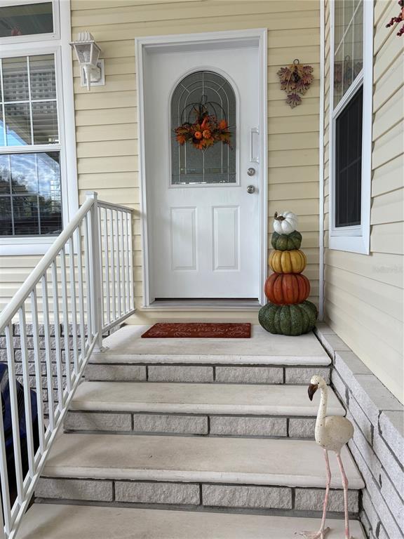 A white front door with a decorative wreath sits above concrete steps with seasonal decor — 11147 102ND WAY UNIT 212, LARGO, FL
