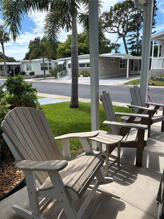 A covered porch features three Adirondack-style chairs and a small table overlooking a residential street — 11147 102ND WAY UNIT 212, LARGO, FL