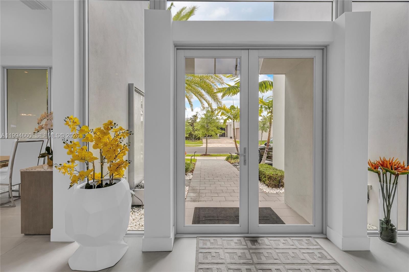 A bright entryway features glass double doors, a white geometric planter, and a patterned rug — 16631 Sunset Way, Weston FL 33326, WESTON, FL