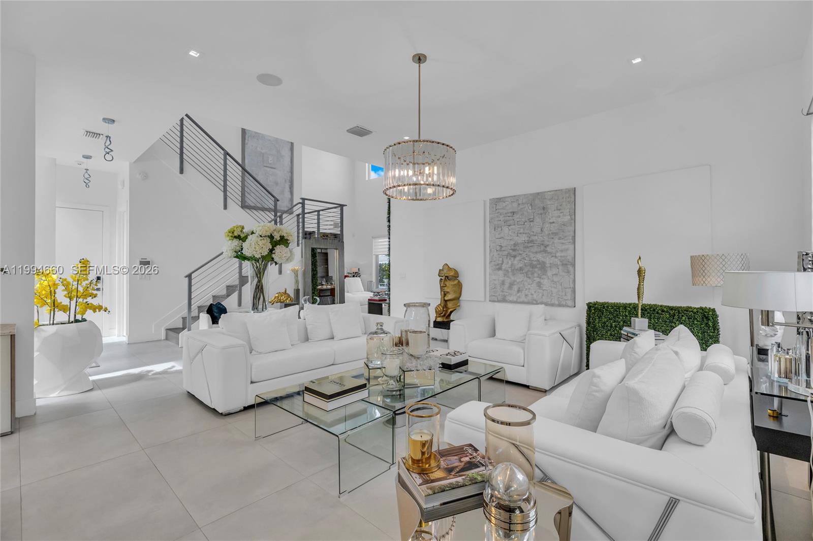A bright, modern living room features white leather sofas, a glass coffee table, and a staircase — 16631 Sunset Way, Weston FL 33326, WESTON, FL