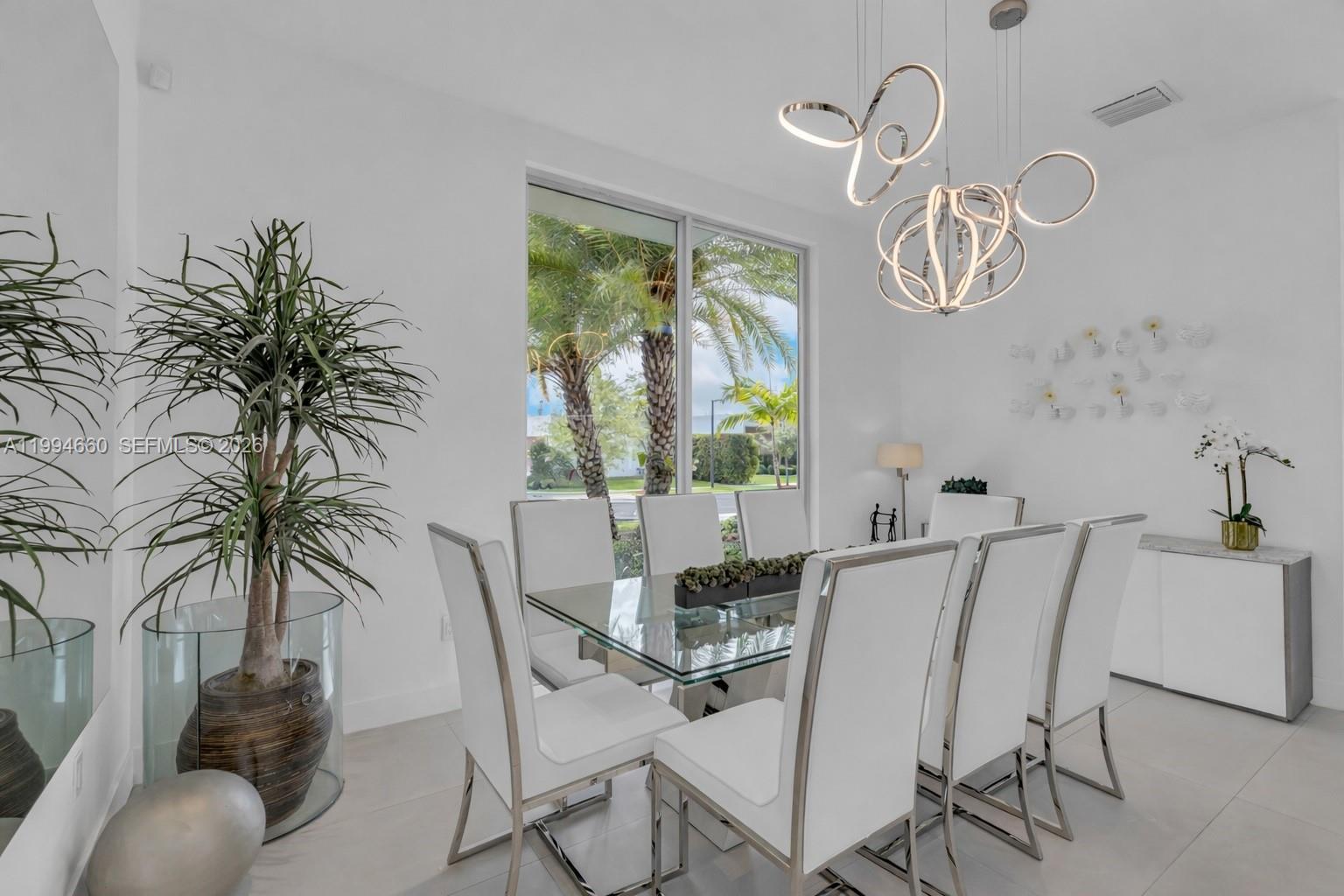 A modern dining room features a glass table, white chairs, and a sculptural chandelier — 16631 Sunset Way, Weston FL 33326, WESTON, FL