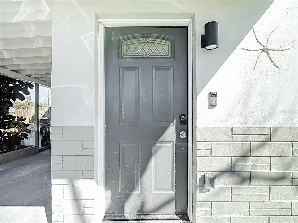 A gray front door with a small window sits between white walls and brick siding — 6726 DEL PRADO TERRACE, NEW PORT RICHEY, FL