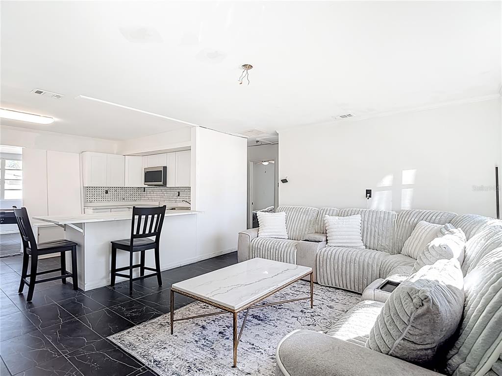 An open-concept living room and kitchen featuring white cabinetry, a marble-topped coffee table, and tile flooring — 6726 DEL PRADO TERRACE, NEW PORT RICHEY, FL