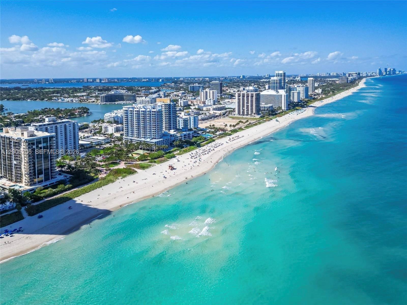 An aerial view shows a sandy beach along a turquoise ocean with high-rise buildings nearby — 6515 Collins Ave # 1505, Miami Beach FL 33141, MIAMI BEACH, FL