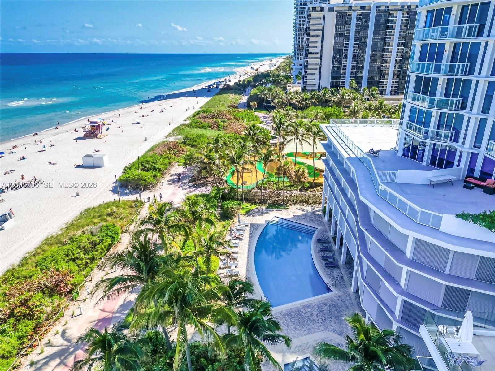 An aerial view shows a swimming pool, palm trees, a sandy beach, and high-rise buildings — 6515 Collins Ave # 1505, Miami Beach FL 33141, MIAMI BEACH, FL