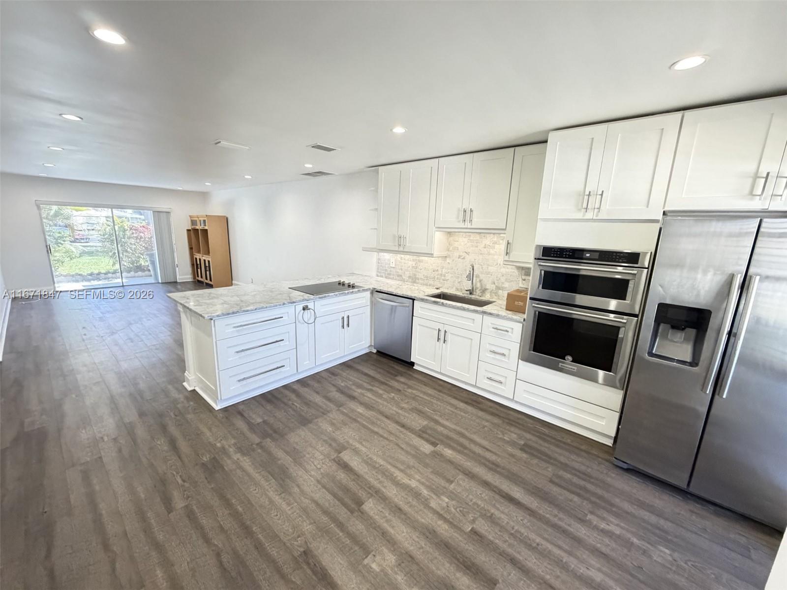 A modern kitchen features white cabinets, stainless steel appliances, and gray wood-look flooring — 20927 Sedgewick Dr, Boca Raton FL 33433, BOCA RATON, FL