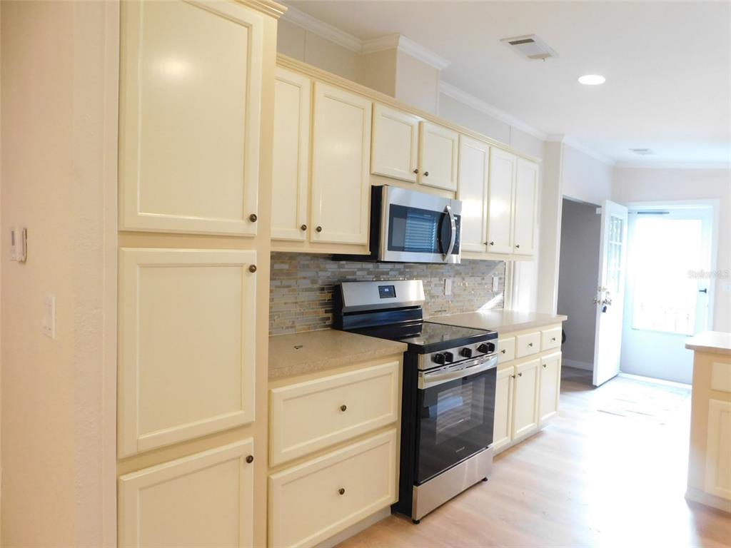 A kitchen features cream-colored cabinets, stainless steel appliances, and a mosaic tile backsplash — 200 COLUMBIA STREET, ARCADIA, FL