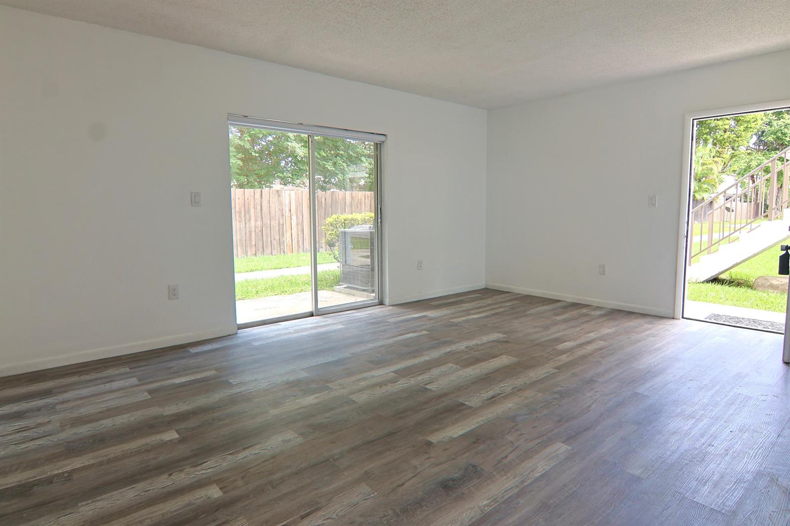 An empty living room with wood-look flooring, white walls, a sliding glass door, and exterior access — 6931 SW 129th Avenue # 3, Miami FL 33183, MIAMI, FL