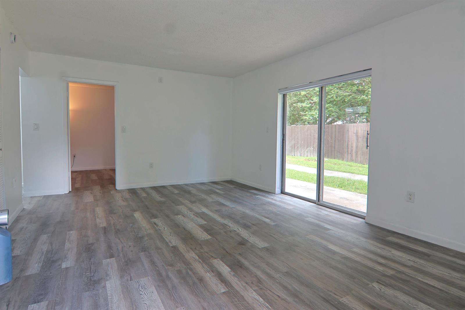 An empty living room with wood-look flooring, white walls, and a sliding glass door — 6931 SW 129th Avenue # 3, Miami FL 33183, MIAMI, FL