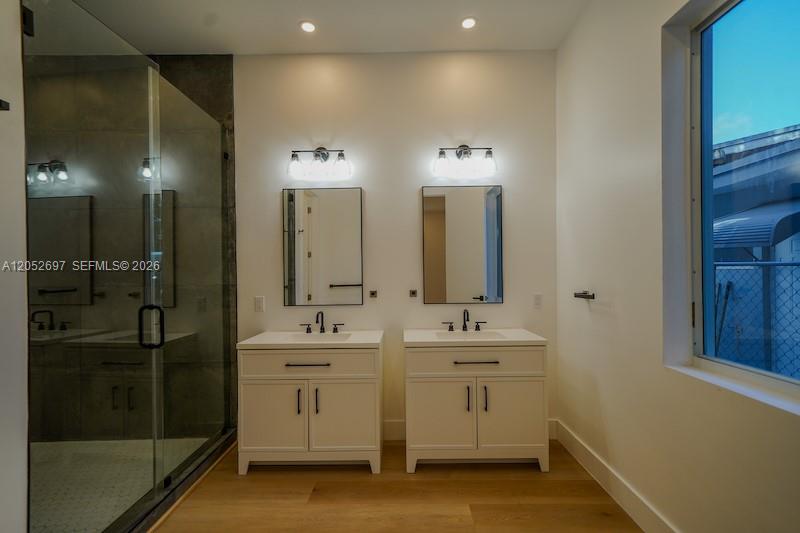 A modern bathroom features a glass-enclosed shower, dual white vanities, and light wood flooring — 112 NW 24th Ct, Miami FL 33125, MIAMI, FL