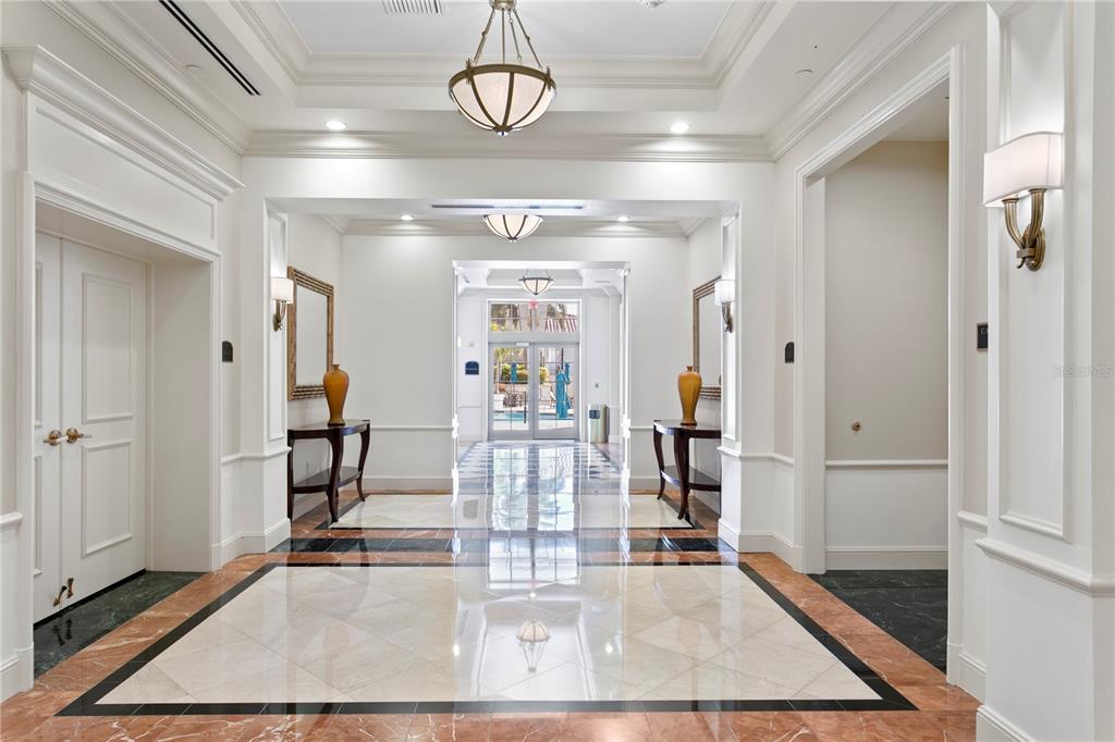 A bright, symmetrical lobby features polished marble floors, decorative light fixtures, and a glass-paned doorway — 300 BEACH DRIVE NE UNIT 1201, ST PETERSBURG, FL