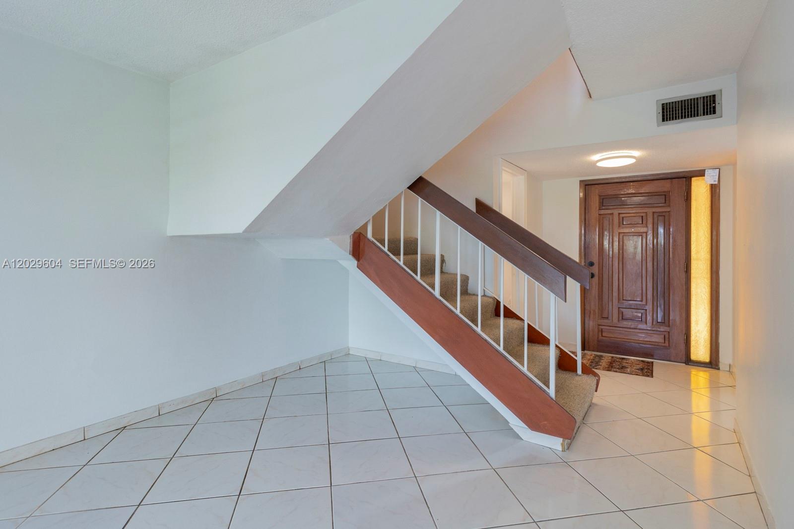 An entryway features white tile flooring, a carpeted staircase with a wooden handrail, and a door — 3804 SW 79th Ave # 76, Miami FL 33155, MIAMI, FL