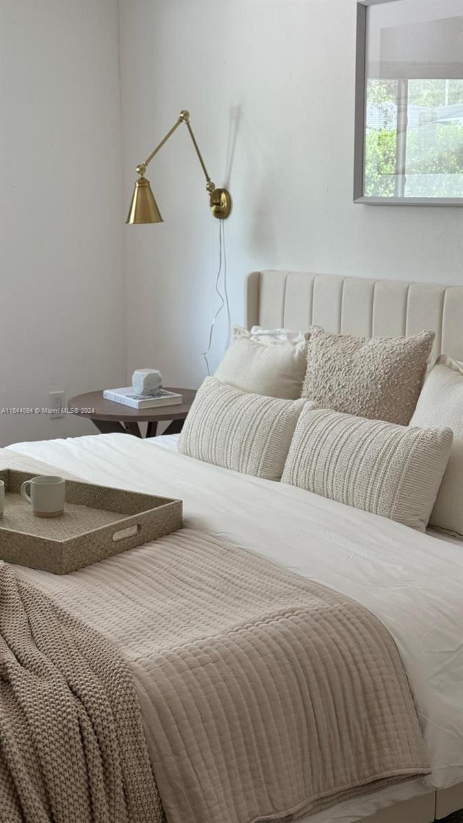 A bedroom features a neutral-toned bed with textured pillows, a bedside table, and a wall sconce — 630 NE 117th St, Biscayne Park FL 33161, BISCAYNE PARK, FL