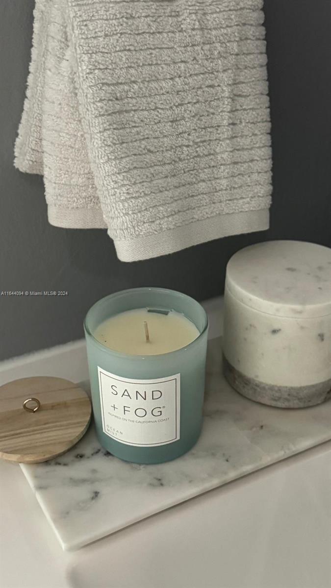 A Sand + Fog candle sits on a marble tray next to a white towel — 630 NE 117th St, Biscayne Park FL 33161, BISCAYNE PARK, FL