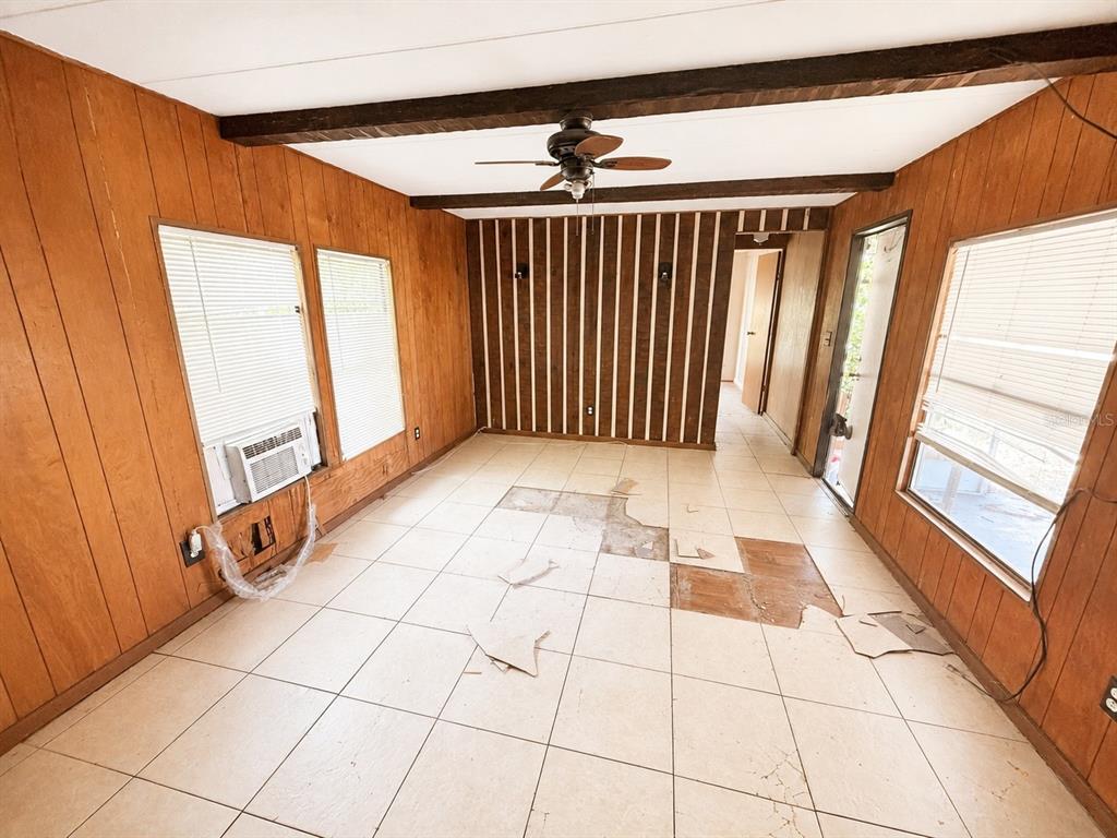 A room with wood-paneled walls, a ceiling fan, and damaged tile flooring — 9136 SW 31ST AVENUE ROAD, OCALA, FL