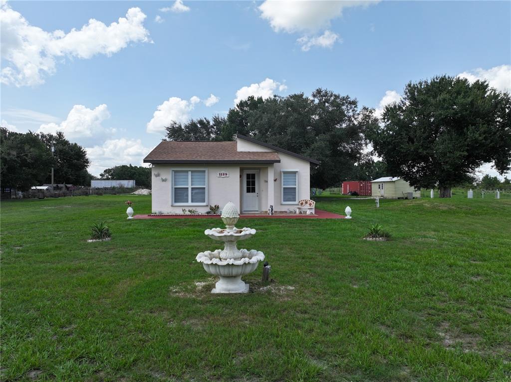 A single-story house with a white exterior and a front fountain sits on grass — 1129 HOPKINS LANE, ZOLFO SPRINGS, FL