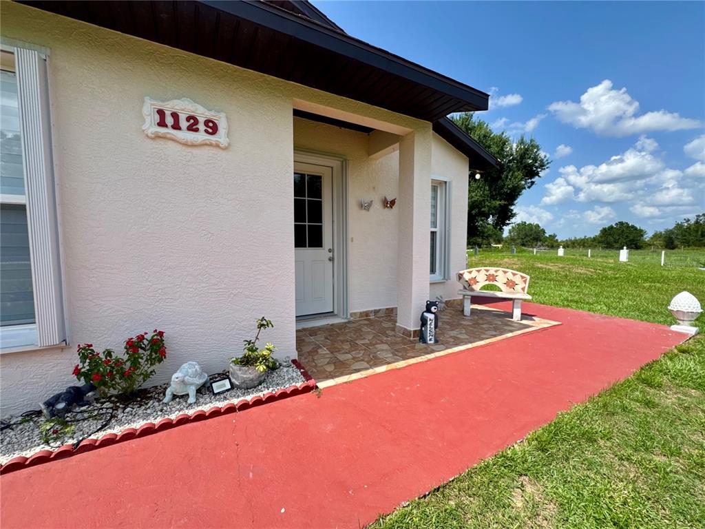 A house exterior features a red walkway leading to a covered porch with a bench — 1129 HOPKINS LANE, ZOLFO SPRINGS, FL